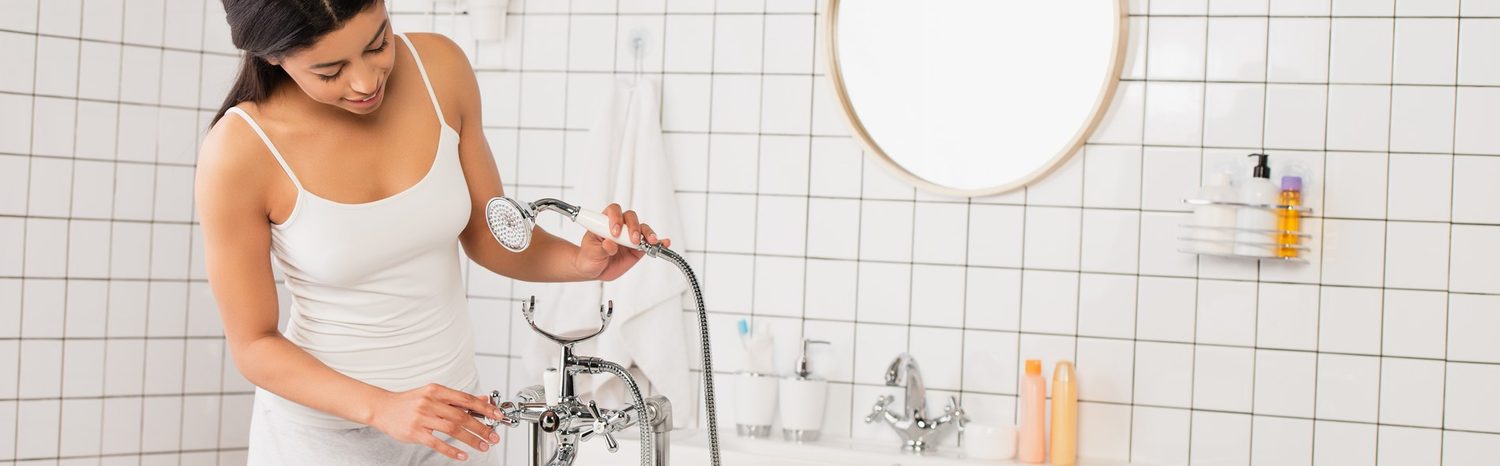 Frau prüft einen Handduschkopf über der Badewanne
