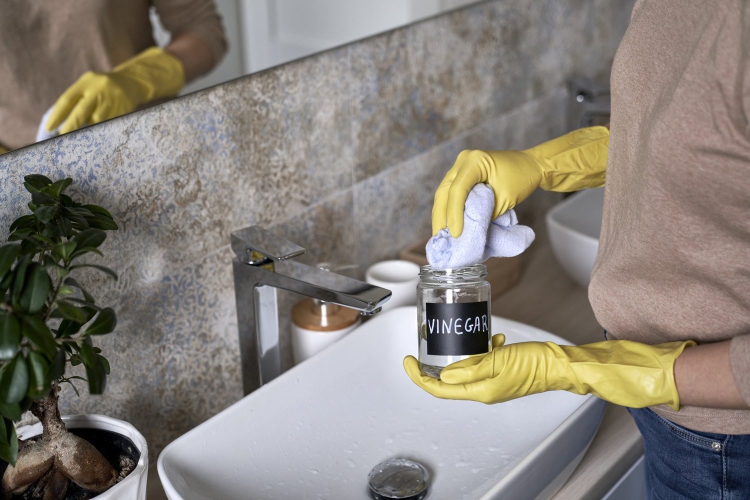 Frau mit Essigglas und Reinigungstuch am Waschbecken im Badezimmer