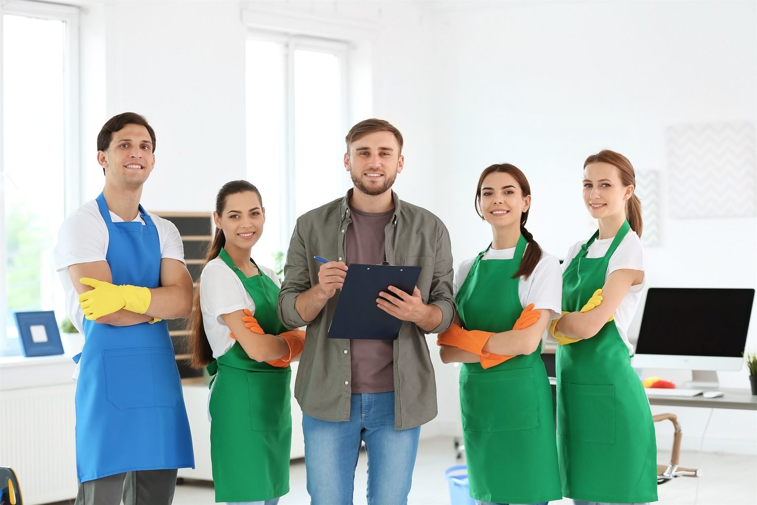 Fünf Mitglieder eines Reinigungsteams stehen in einem hellen Büro; der Mann in der Mitte hält ein Klemmbrett.