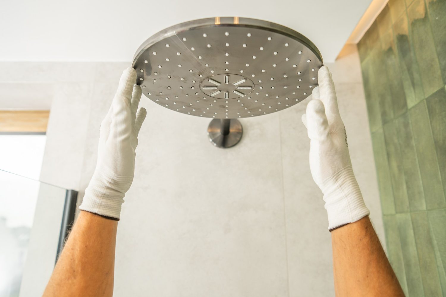 Hände mit weißen Handschuhen montieren einen neuen Duschkopf im Badezimmer