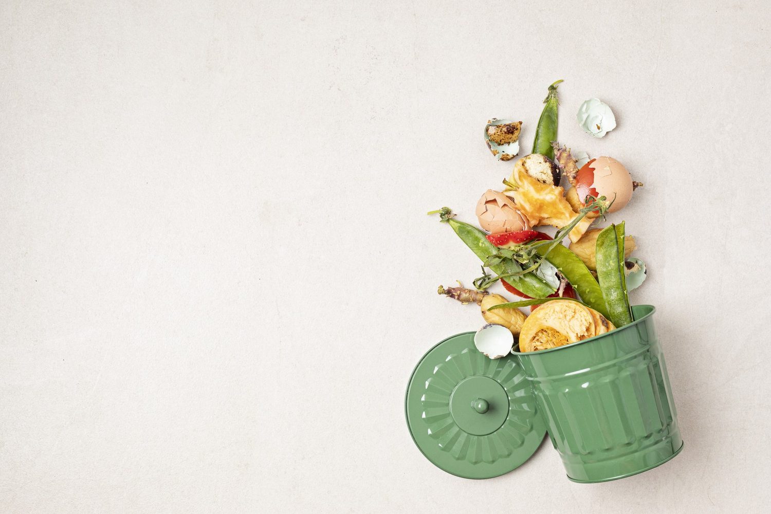 Aus einem umgekippten grünen Mülleimer fallen Obst- und Gemüsereste