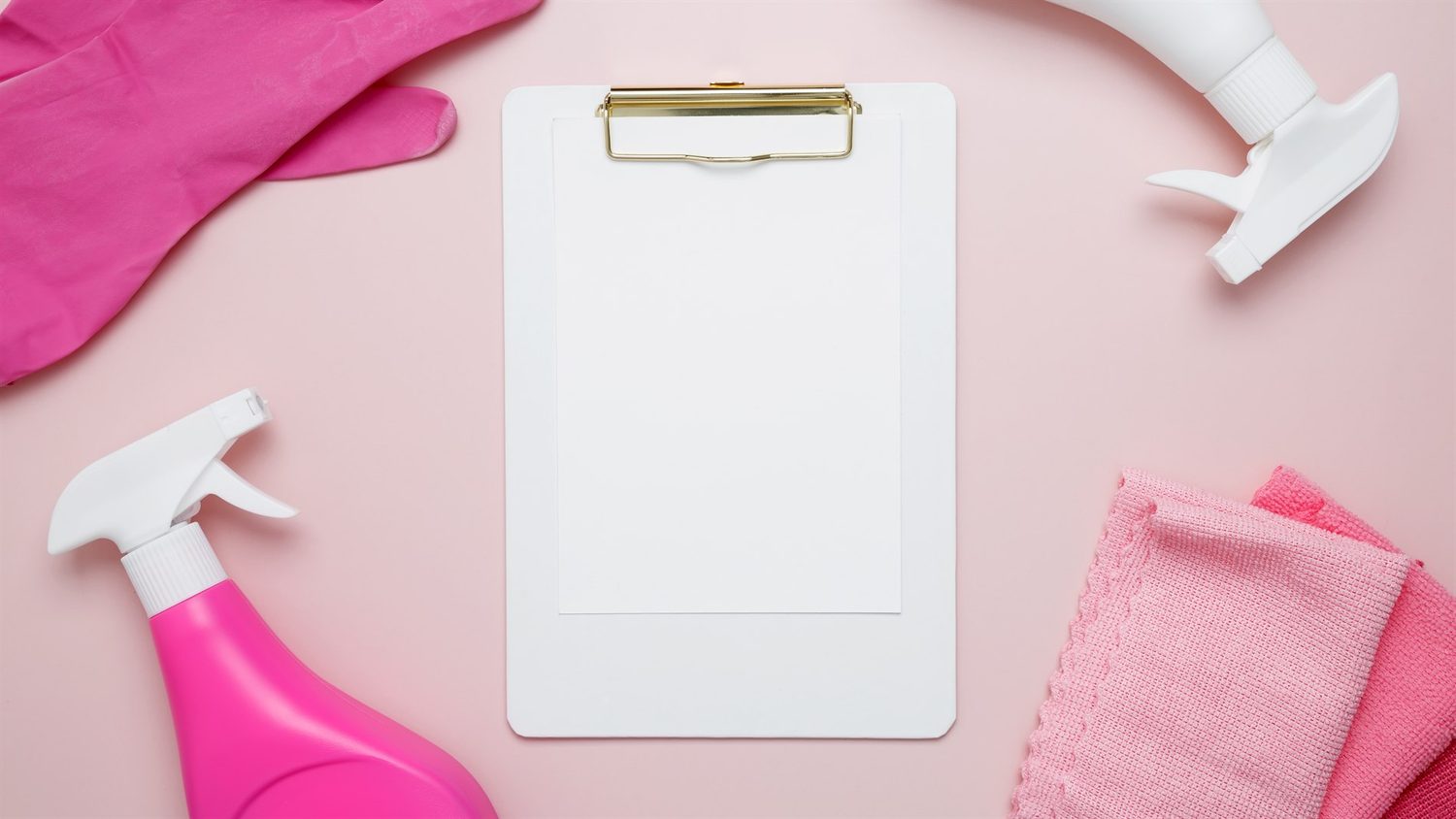 Ein leeres Klemmbrett liegt zwischen rosa Reinigungshandschuhen, Sprühflaschen und Tüchern auf rosafarbenem Untergrund.