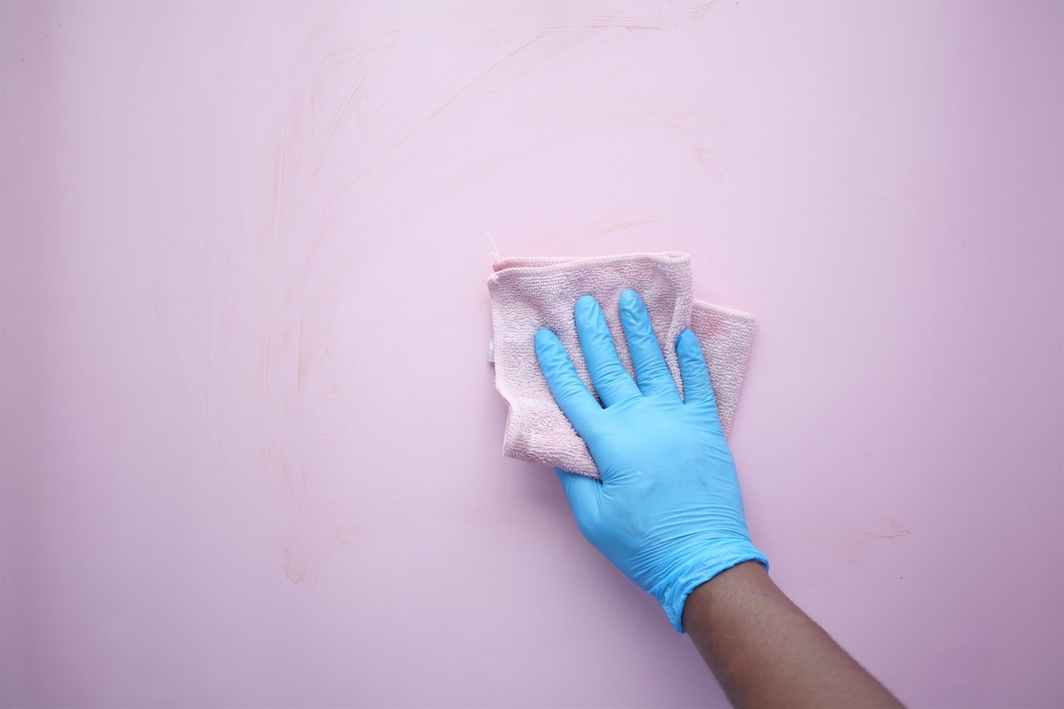 Eine Hand mit blauem Handschuh wischt eine rosa Wand mit einem weichen Tuch ab.