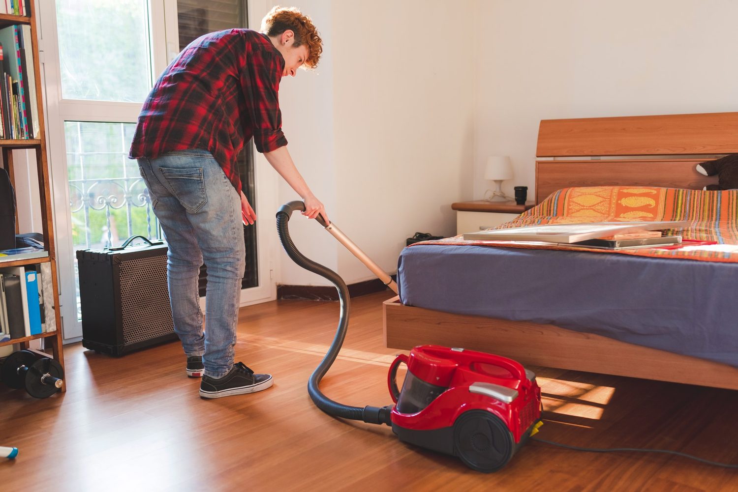 Person saugt den Holzboden im Schlafzimmer neben dem Bett