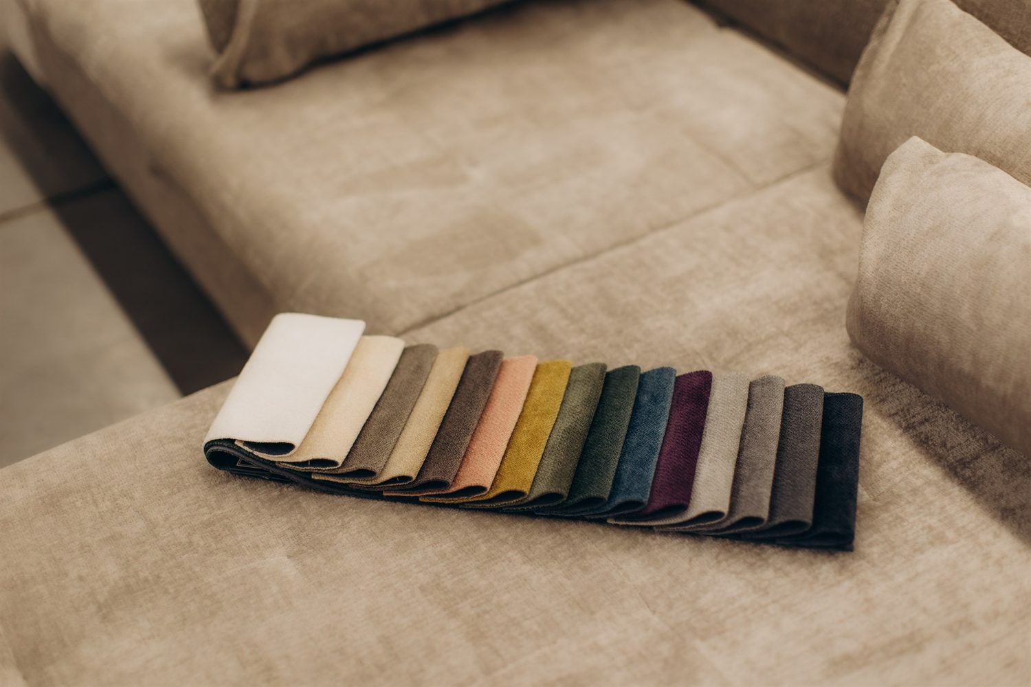 Stoffmuster in verschiedenen Farben liegen nebeneinander auf einem beigen Sofa.