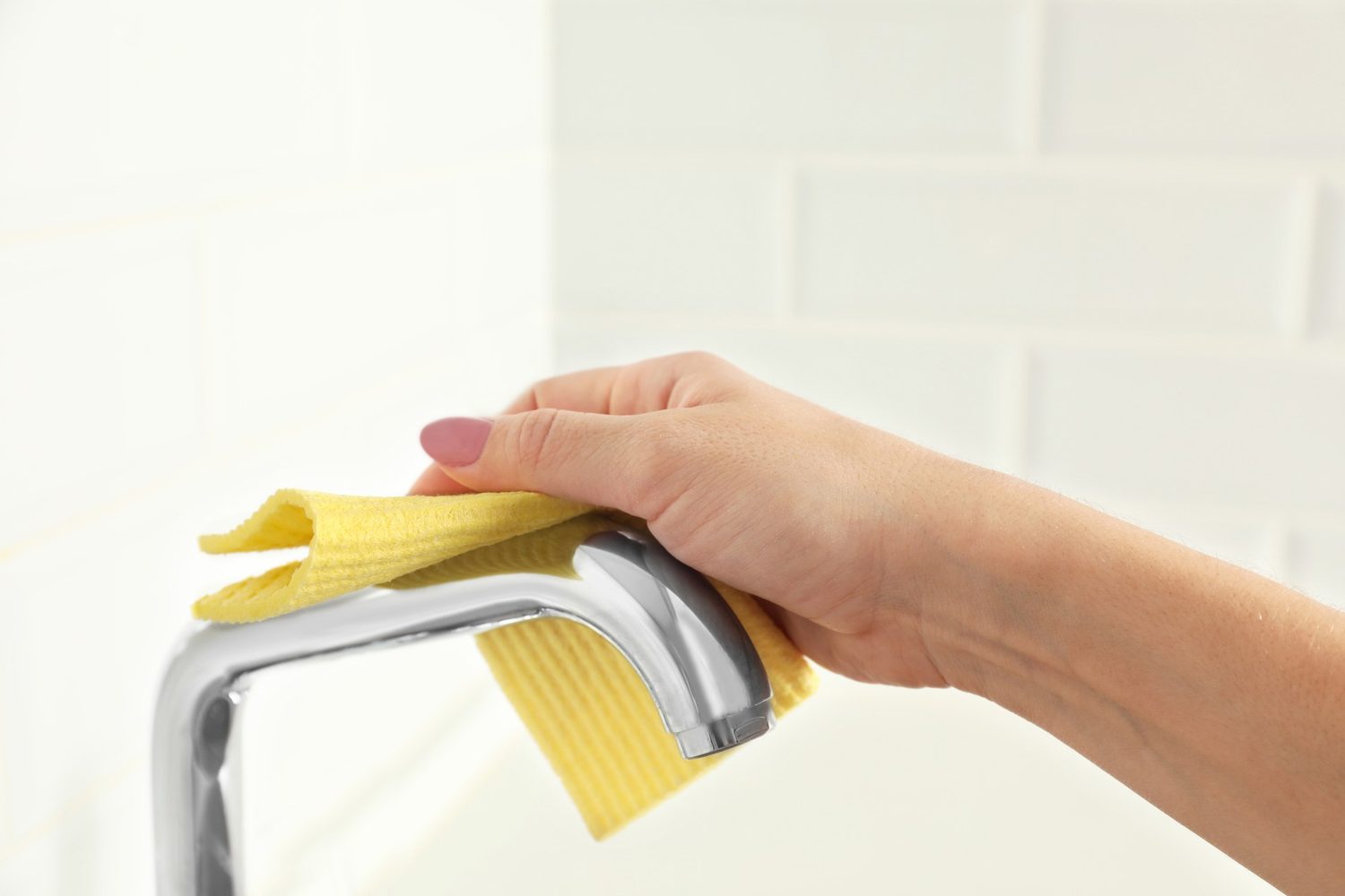 Hand wischt einen verchromten Wasserhahn mit einem gelben Tuch trocken