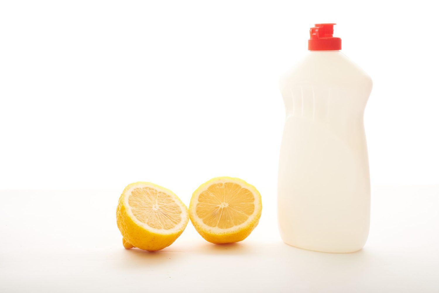 Zwei Zitronenhälften neben einer Flasche mit Flüssigkeit auf weißem Hintergrund.